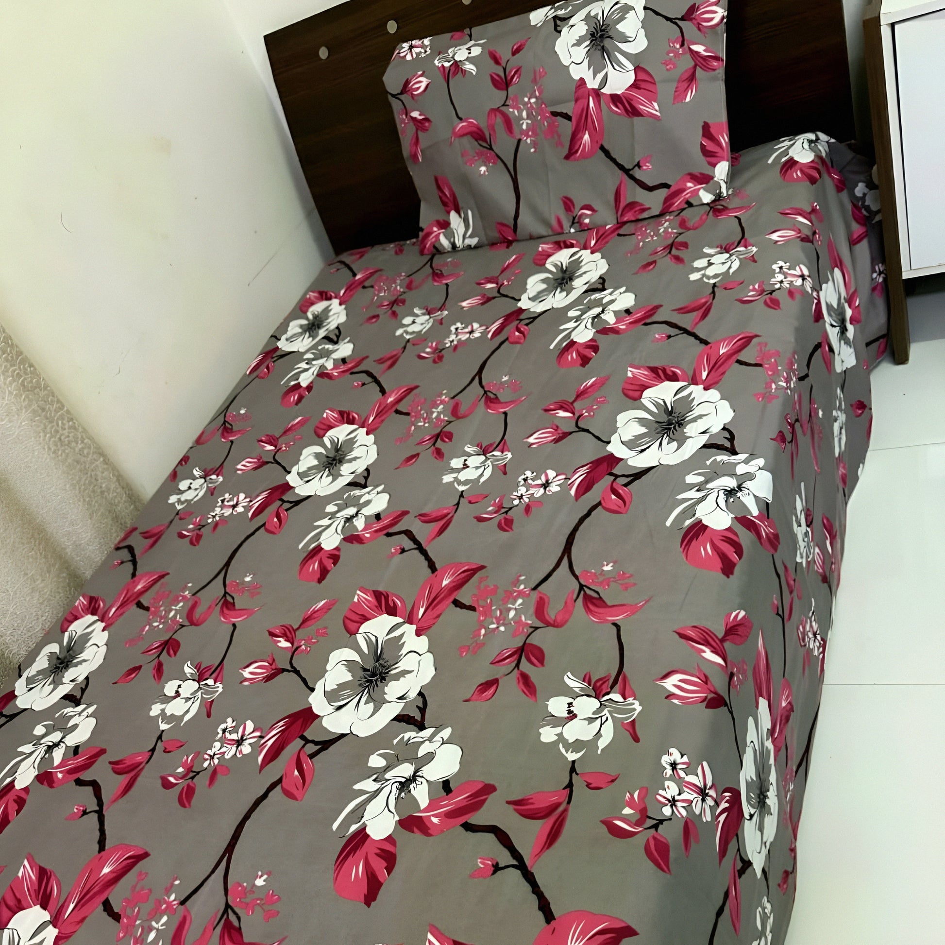 Pink floral bedsheet with white blossoms on grey background, styled on a single bed — Marjan3x UAE